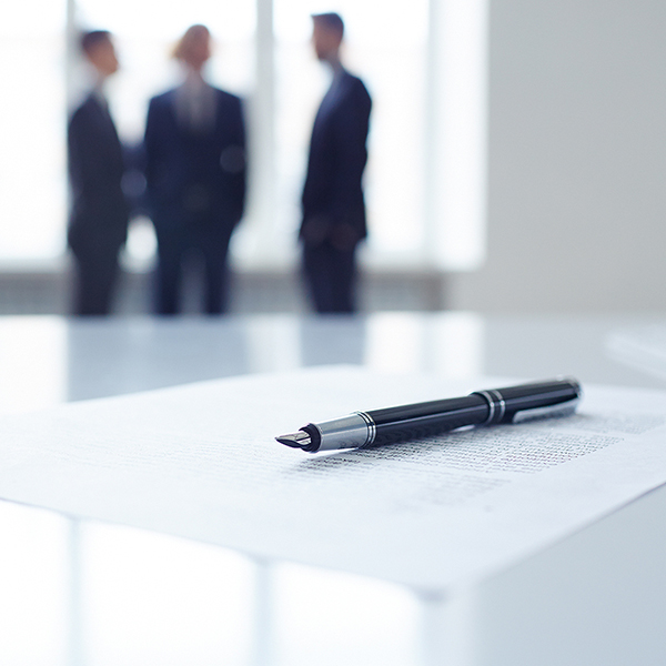 Image of business document, pen and glass of water at workplace with group of colleagues on background